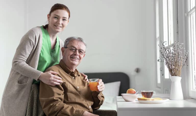 Caregiver smiling with senior resident enjoying morning juice in a bright, home-like room at Lakeway Copperleaf Homestead assisted living